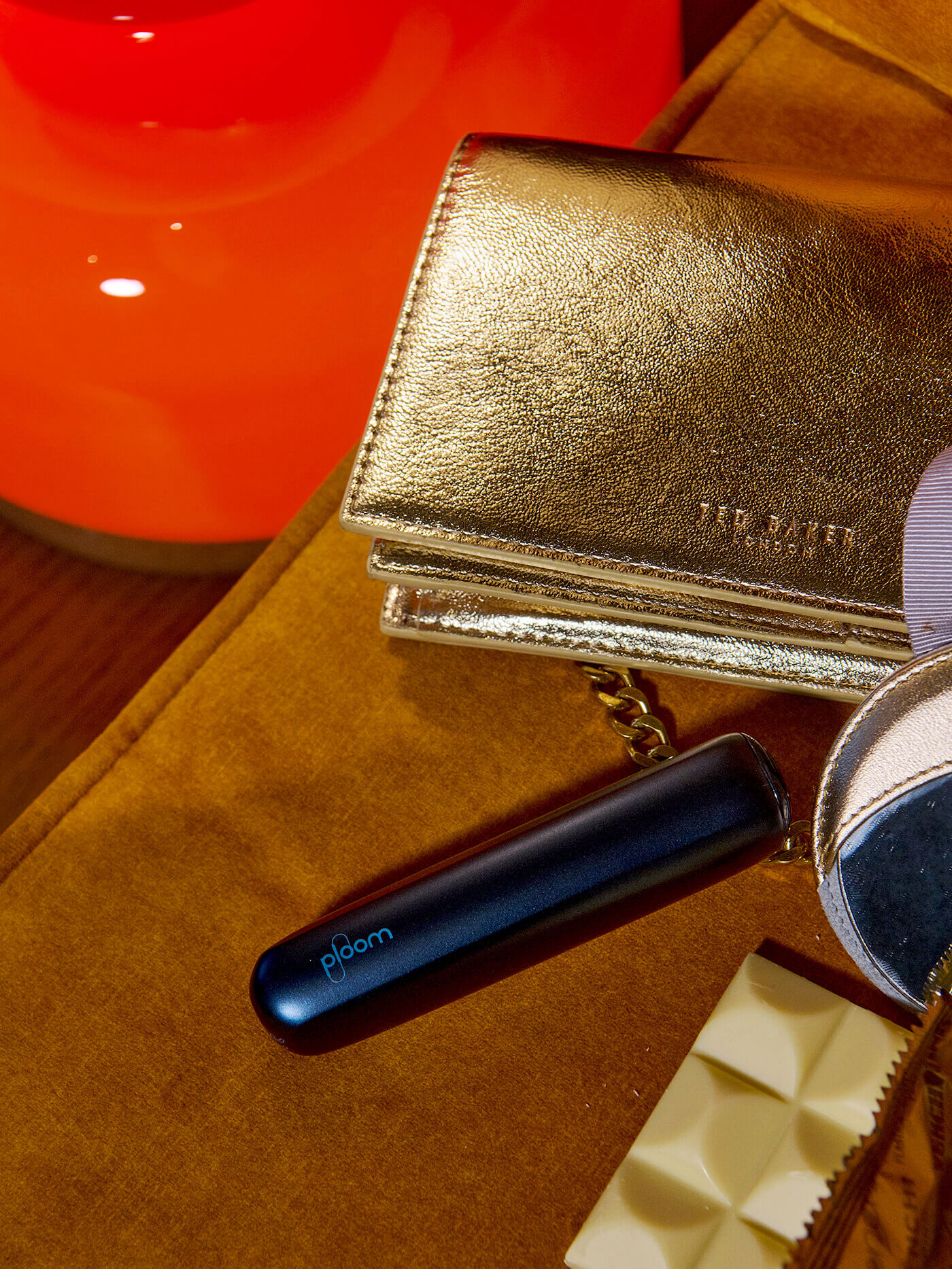 Χρυσό clutch και συσκευή Ploom Aura σε ζεστό φόντο