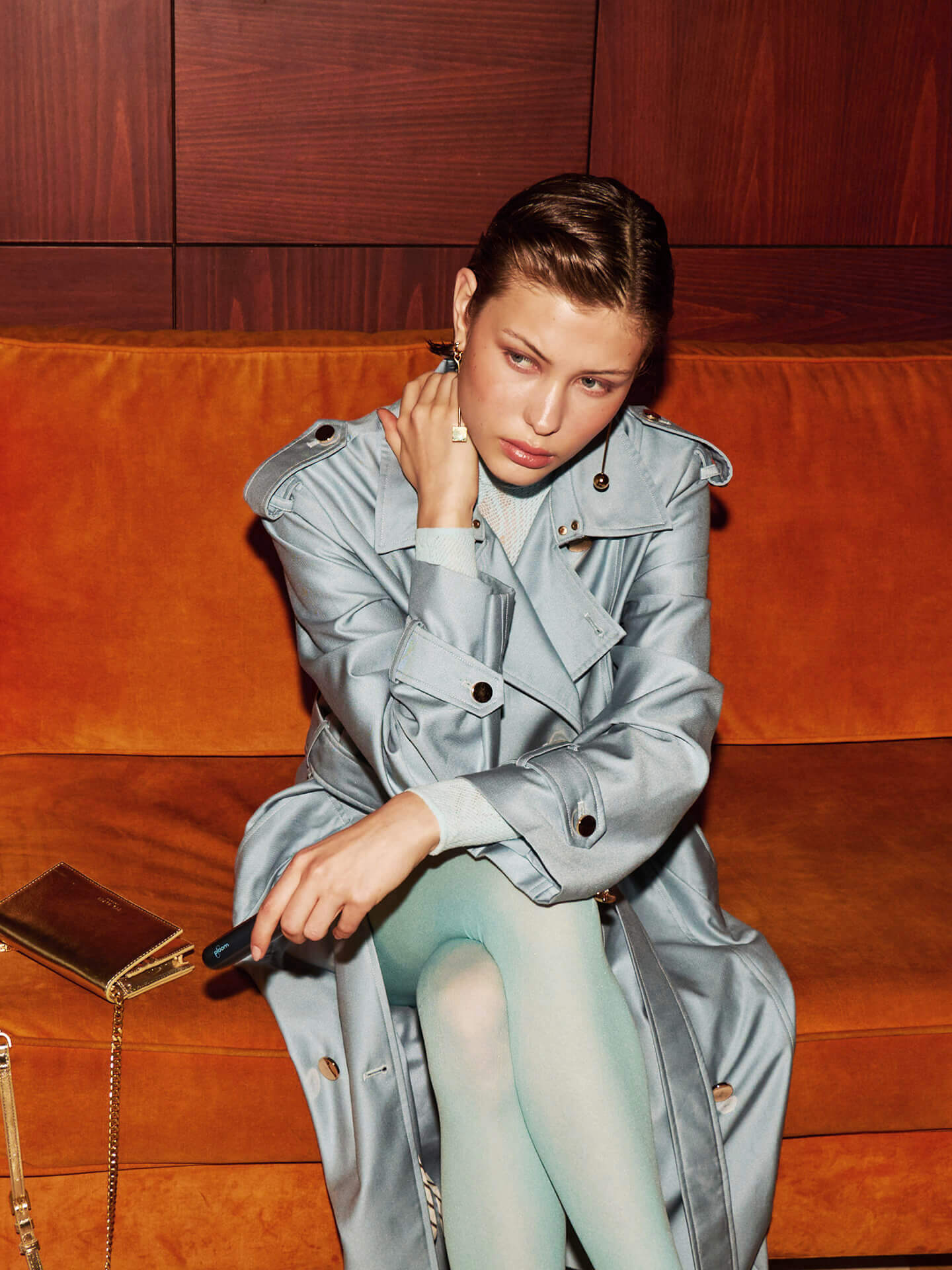 Γυναίκα με παλτό σε καναπέ κρατά τη συσκευή Ploom Aura